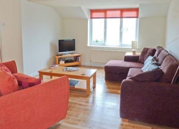 Lounge with sn L-shaped sofa seating four an armchair, coffee table and TV.