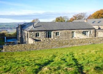 A single storey stone cottage sits behind a low stone wall.