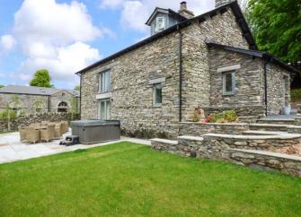 Stone-built estate cottage with a hot tub on its patio and a large lawn.