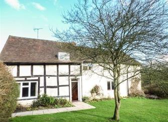 A crossed-timbered Herefordshire country cottage with a lawned containing a mature tree.