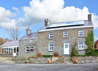 A detached, double fronted, stone-built cottage with a front garden behind a low stone wall.