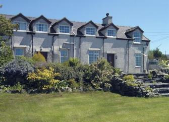 A row of terraced houses look down over a flower-filled rockery to a large lawn.