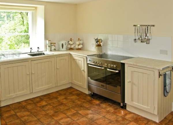 A kitchen corner with fitted units on a terracotta tiled floor  and an electric cooker with twin ovens below a ceramic hob.