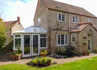 Exterior of a stone cottage with enclosed porch and sun lounge overlooking a lawn.