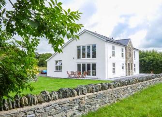 A large house with floor-to-ceiling windows surrounded by a large garden in the countryside.