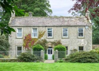 A classic country house with a row of five windows overlooks a shrub0filled garden lined by wrought iron railings. 