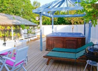 A hot tub beneath a glass roof sits on a wooden deck next to two sun loungers.
