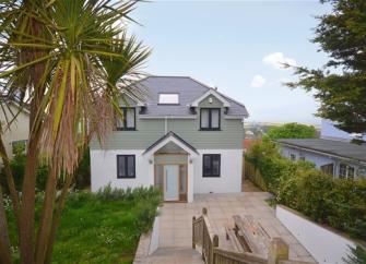 A modern, 2-storey, half-timbered house overlooks a long garden and paved terrace lined by palm trees.