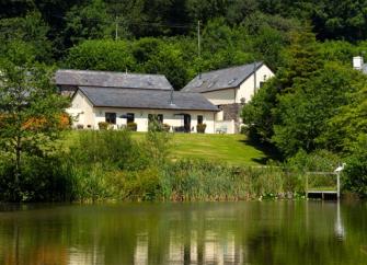 A row of barn conversions are reflected in the surface of a lake.