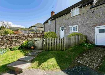 Exterior of a stone-built terraced cottage with a picket fence around the front garden.