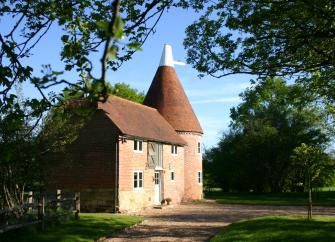 An oast house converted to a holiday cottage in Suffolk surrounded by trees on a sunny summer's day