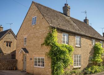 A semi-detached Cotswold honeystone cottage with wisteria-clad walls