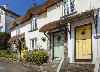 Exterior of a small terrace of thatched cottages overlooking a quiet North Devon village.