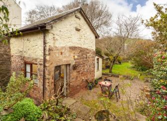 A stone-built Quantock Hills holiday cottage overlooks a garden with cobbled patio, shrubs and bushes.