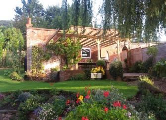 Exterior of a single storey holiday apartment with a vine covered pergola and floral garden.