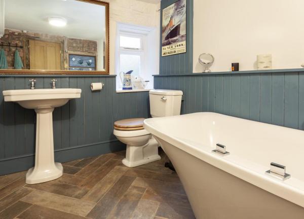 A wood-floored bathroom with a bath, WC, washbasin with large wall mirror above.