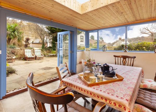 A sun room with open bi-fold doors ro a patio contains a dinner table seating 8.