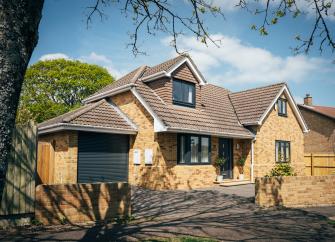 Exterior of a contemporary New Forest chalet bungalow bordered by trees on a sunny day in summer.