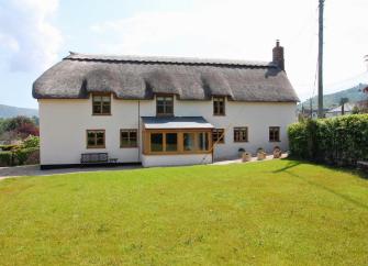 A traditional Somerset cottage with white rendered walls and a newly thatched roof overlooks a large lawn