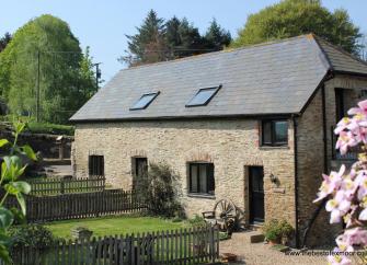 Exterior of a sonte-buklt Exmoor holiday cottage with a background of trees and a clear sky
