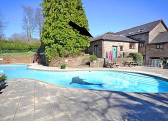 A stone built cottage overlooks a large outdoor swimming pool surrounded by wide terraces