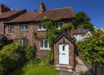 Exterior of a wisteria-clad stone-built holiday cottage in Porlock on a sunny day.
