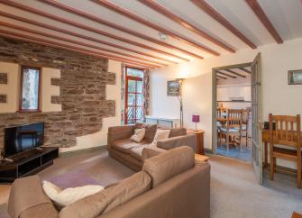 A holiday cottage lounge with exposed stone walls, pine beams and comfortable sofas.