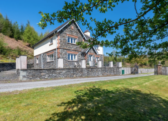 Exterior of a large stone-built house with big gable ends overlooking an empty road and lawns.