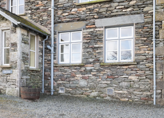 stone-built exterior of a large Cumbrian holiday lodge with rows of windows and a stone porch.