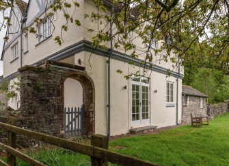 Exterior of a farmhouse in Cumbriaamidst mature trees and a large lawn.