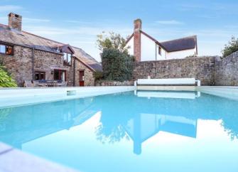 An outdoor swimming pool oerlooked by a stone-buiolt holiday cottage in North Devon