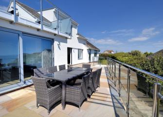 A terrace with dining facilities overlooked by a long 2-storey contemporary house.