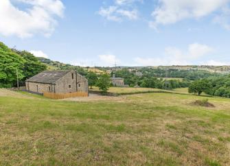 A large barn conversion stands alone in a a Pennine landscape of rough fields and trees.