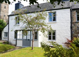 exterior of a two torey cottage with rendered walls and a slate roof overlooking a lawn.