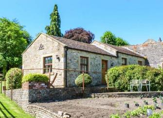 A siungle storey wing of a stone-bult property overlooks a terrace and gardens.