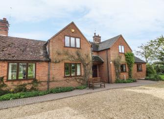 Exteerior of a large brick-built gabled house overlooking a wide drive and lawn