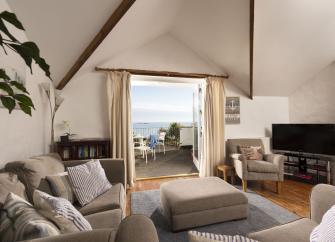 A lounge with tv, coffee table and sofas. French windows to a balcony offer seaviews of Torbay