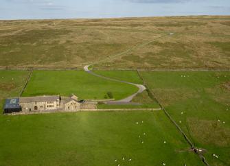 Aerial of moorland countryside with drystone walls and a solitary Pennine farmhouse and outbuildings in the centre.
