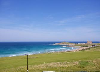 View of a large sandy surfing beach beyond sea front lawns in Newquay