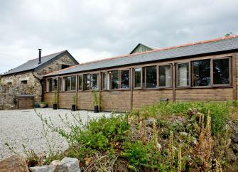 A long single-storey barn conversion with a line of windows along one side overlooks a shingled driveway and garden.
