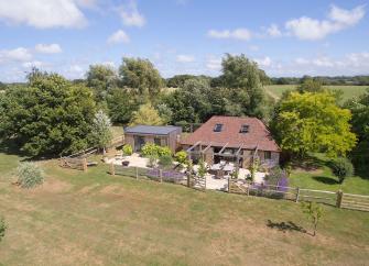 A 2-storey barn conversion with terracotta tiles nestles against a cluster of small trees overlooking a large garden and fields in East Sussex.