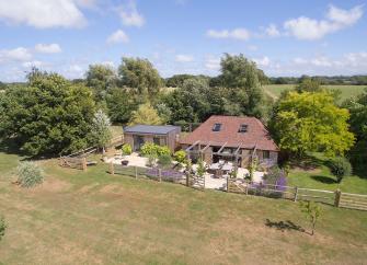 A 2-storey barn conversion with  terracotta tiles nestles against a cluster of small trees overlooking a large garden and fields in East Sussex.