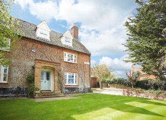Exterior or an old 3-storey country cottage in Norfolk overlooking a large lawn bordered by mature trees.