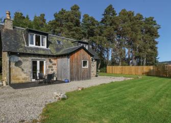 Backed by tall pine trees a 2-storey tone-built Newtonmore holiday cottage overlooks a large lawn.