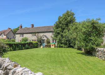 Exterior of a stone-built house overlooking a lawn surrounded by a stone wall and small trees.