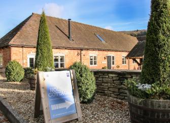 A brick-built barn conversion overlooks a walled courtyard with mature shrubs.