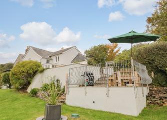 Exterior of a large contemporatry house with a raised terrace and surrounded by mature gardens.