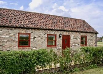 Exterior of a single-storey stone-built rural holiday cottage with a terrace and a front hedge.