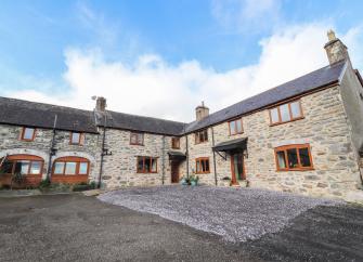 Exterior of a large L-shaped stone farm house overlooking a large courtyard parking area.