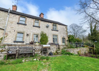 Exterior of a 2-storey stone-built holiday cottage in Derbyshire overlooking a large lawn.